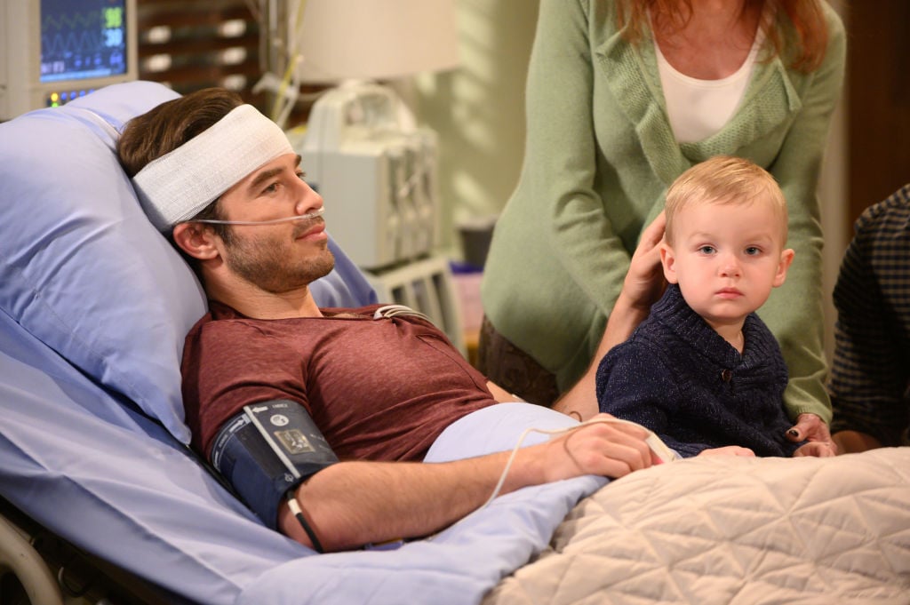 Lucas (Ryan Carnes) in a hospital bed with a baby on his lap