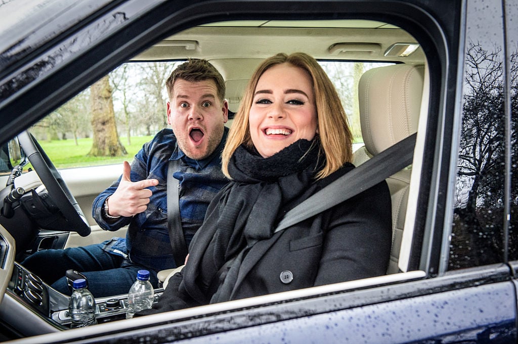 James Corden, in the driver's seat, excitedly pointing at Adele in the passenger seat of a car