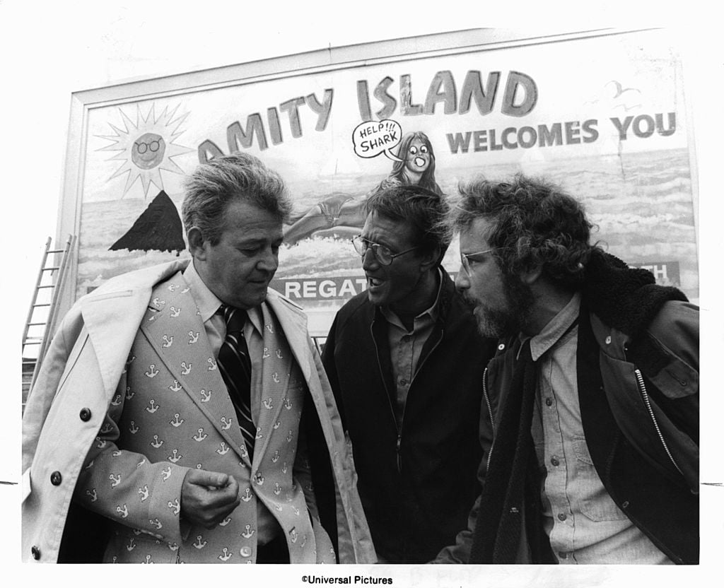 Murray Hamilton, Roy Scheider, and Richard Dreyfuss standing in front of defaced billboard in a scene from the film 'Jaws', 1975