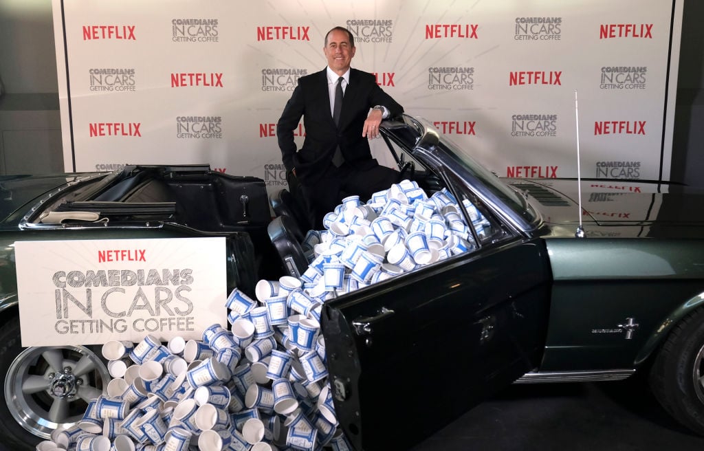 Jerry Seinfeld behind a prop car full of the classic New York to-go paper coffee cups