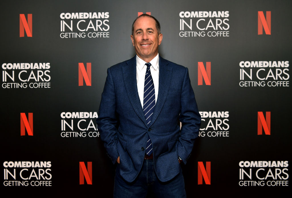 Jerry Seinfeld smiling in front of a repeating background