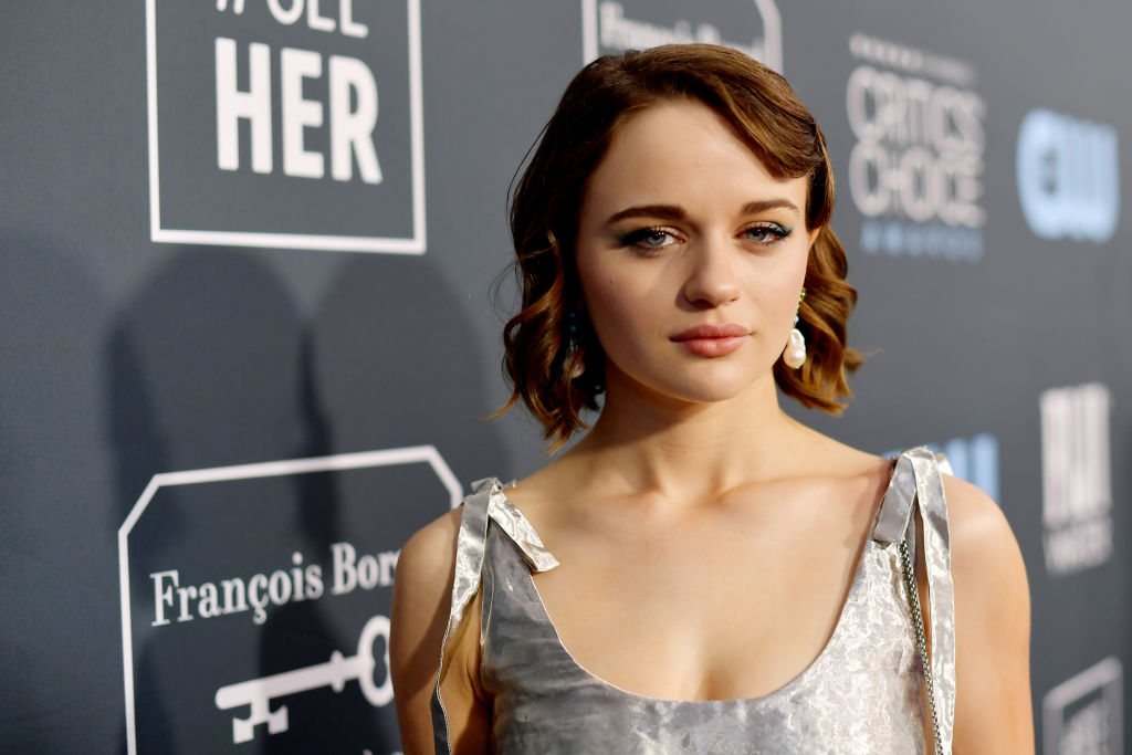 Joey King in front of a repeating background in a silver dress