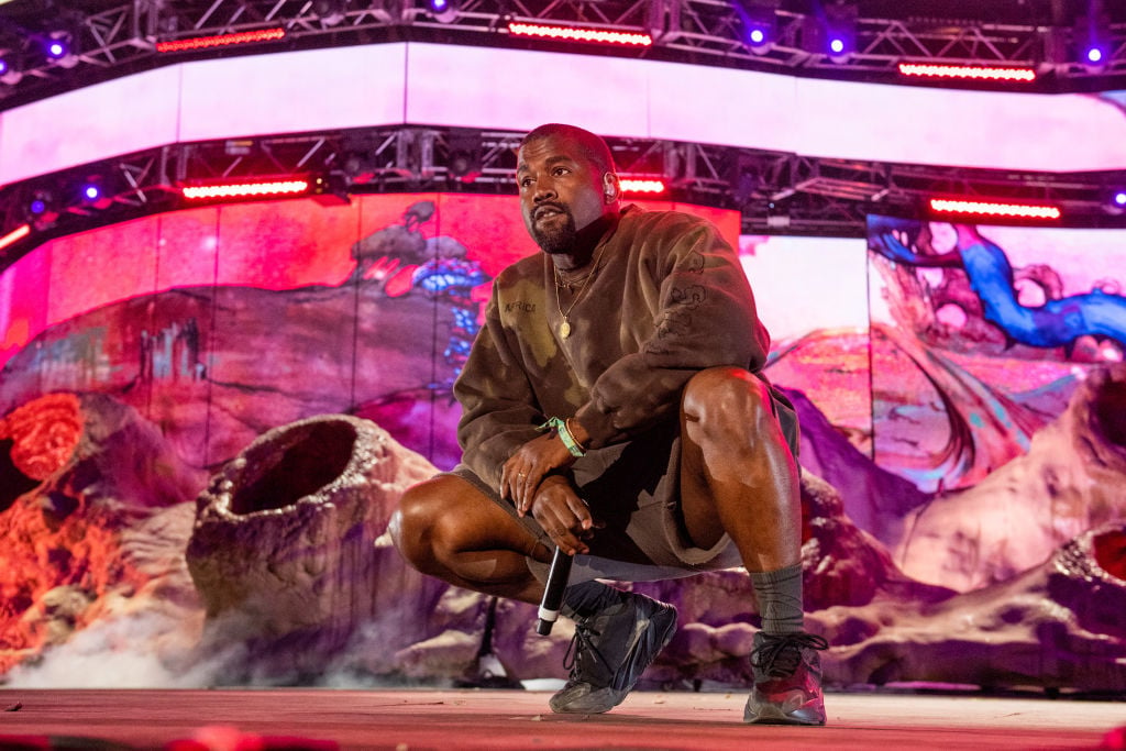 Kanye West crouched down on stage holding a microphone