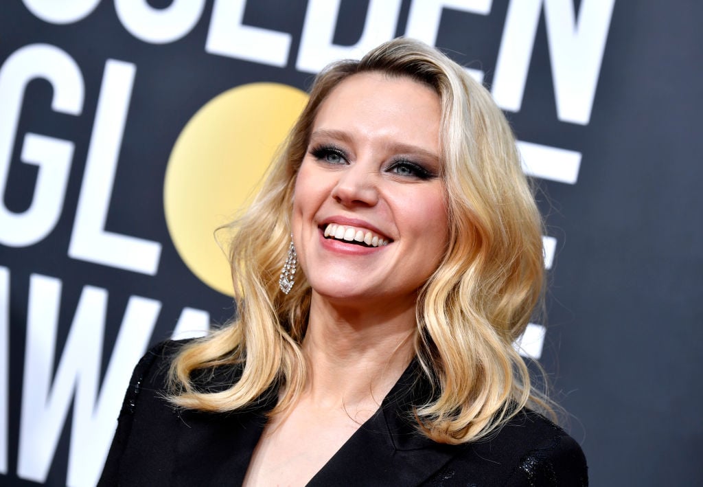 Kate McKinnon smiling in front of a repeating background