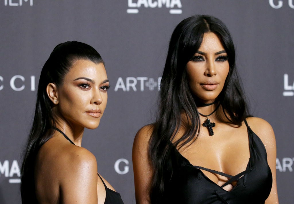 Kourtney Kardashian and Kim Kardashian West in front of a repeating background