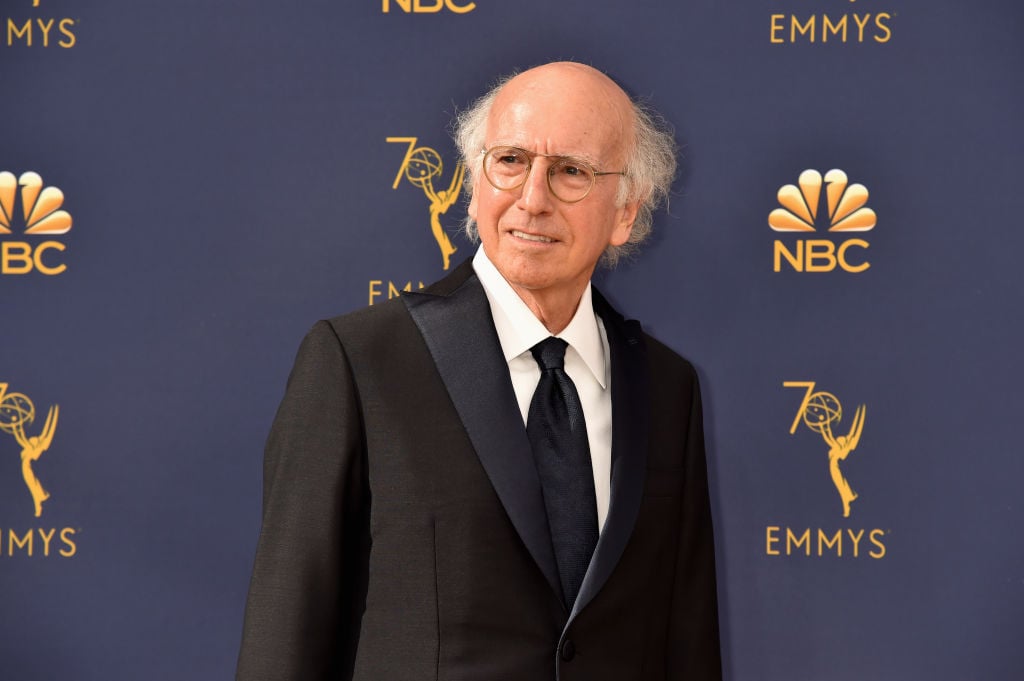 Larry David smiling off camera in front of an Emmy Awards' repeating backdrop