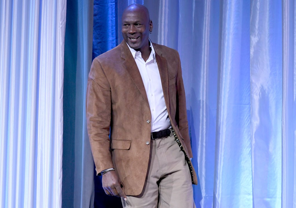 Michael Jordan smiling in a tan suit in front of a white curtain