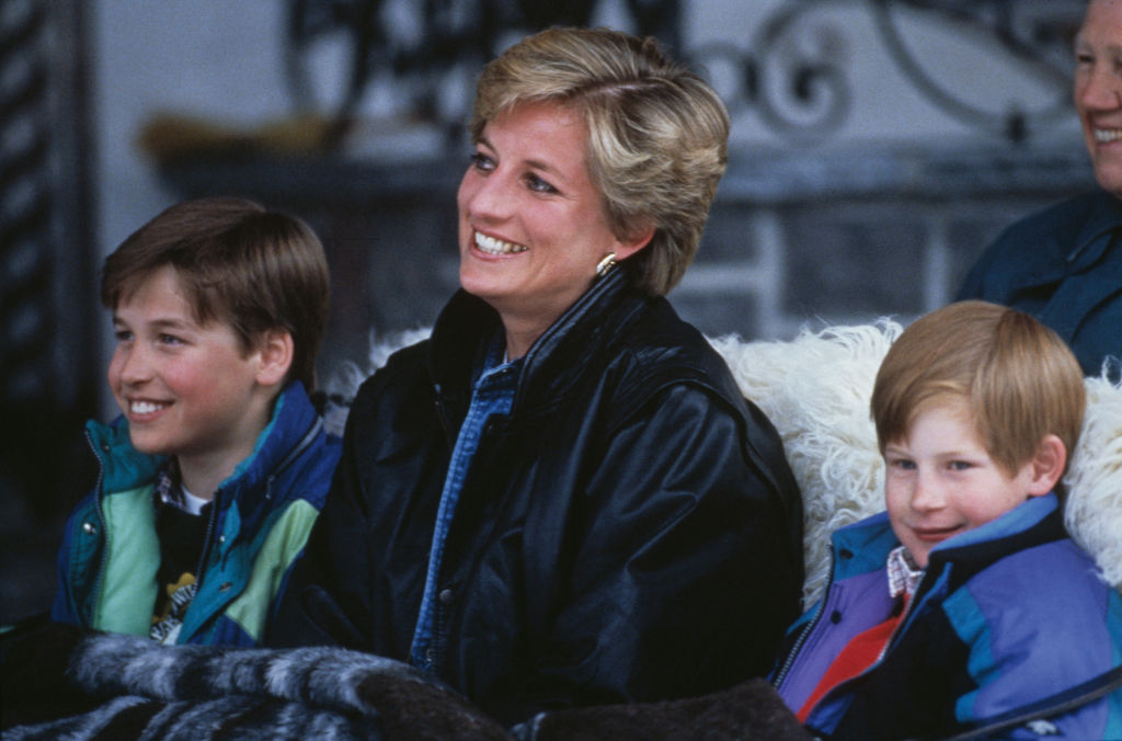 Prince William, Princess Diana and Prince Harry smiling together all wearing winter jackets