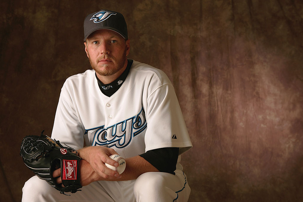 Roy Halladay in Toronto Blue Jays Uniform seated in front of a textured brown background