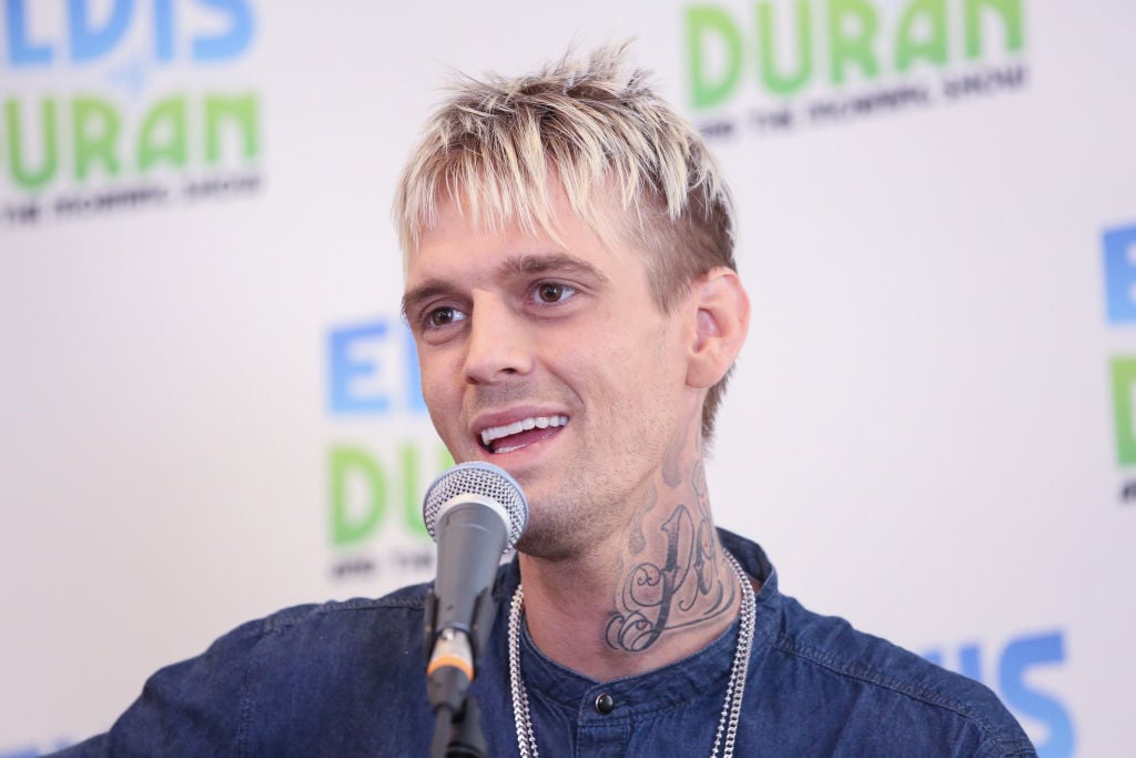 Aaron Carter in front of a microphone in front of a repeating white and blue background
