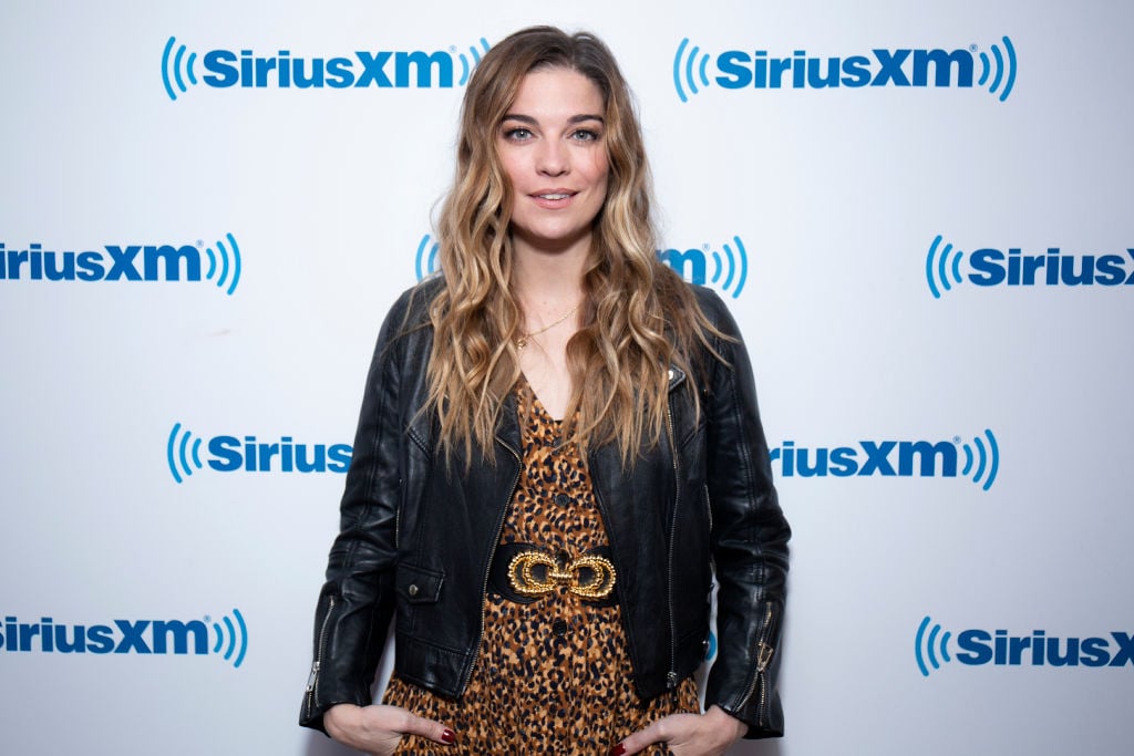 Annie Murphy smiling in front of a white and blue repeating background