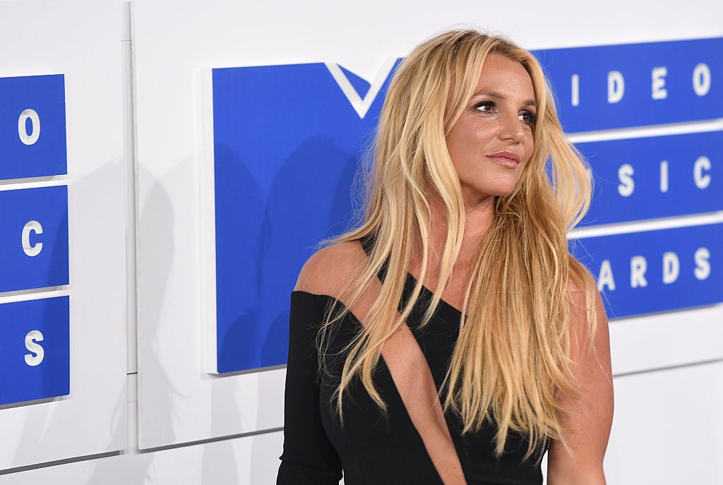 Britney Spears smiling, turned away from the camera in front of a blue and white backdrop