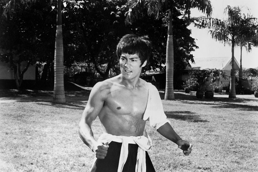 Bruce Lee looking away from the camera, shirtless, with his arms slightly outstretched