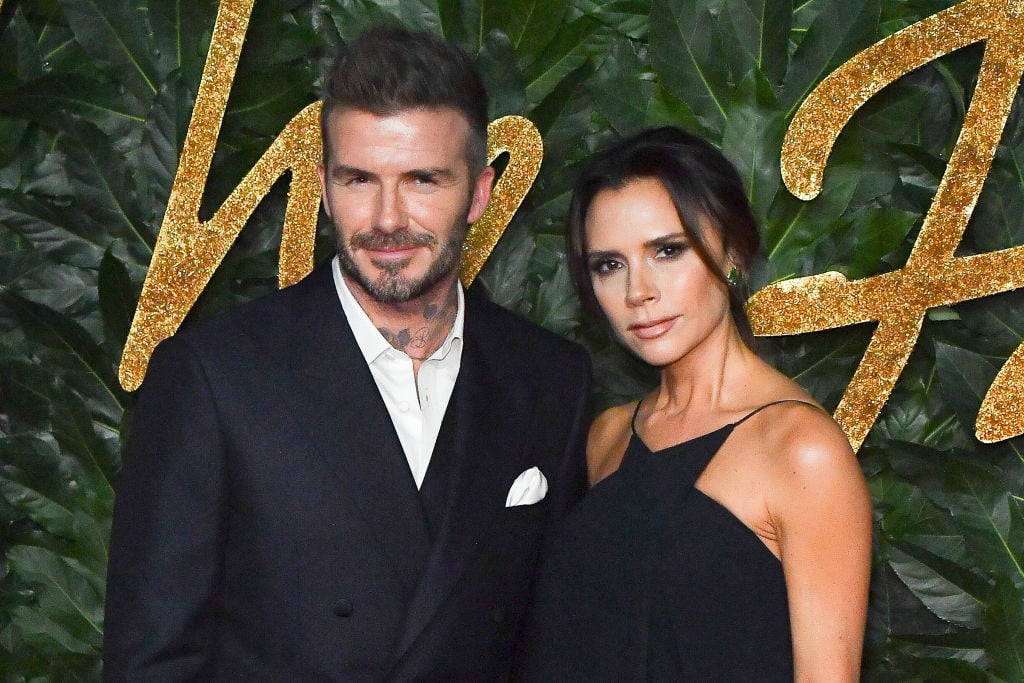 David Beckham and Victoria Beckham smiling in front of a green background