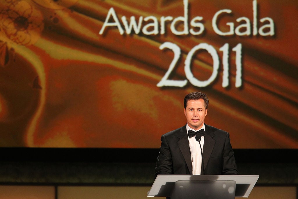 Doug Pitt smiling at a podium for a charity gala