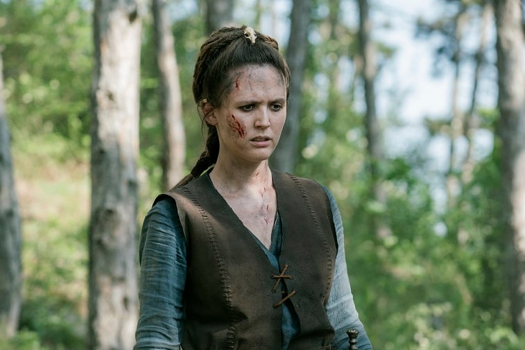 Emily Cox as Brida in 'The Last Kingdom' stands in the woods with blood on her face.