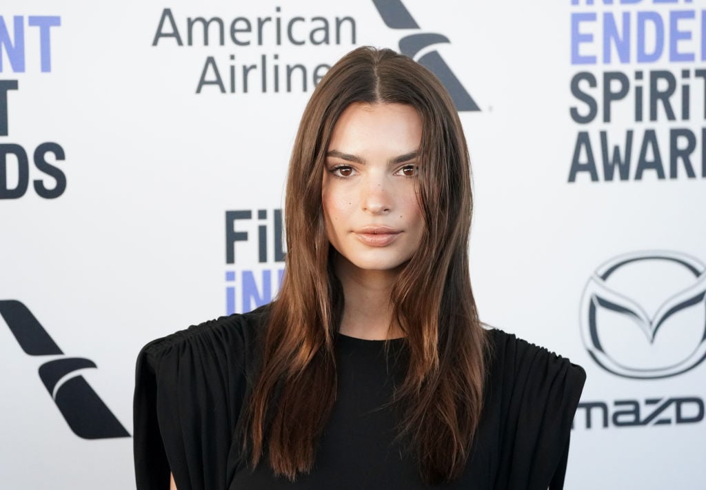 Emily Ratajkowski smiling in front of a repeating black and white background