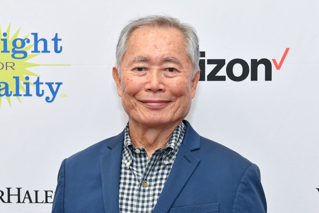 George Takei smiling in front of a repeating background