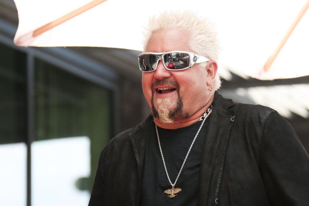 Guy Fieri wearing sunglasses and smiling, facing slightly left