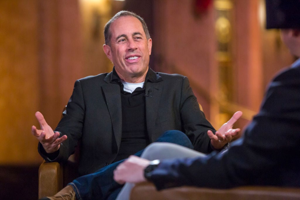 Jerry Seinfeld shrugging, looking away from the camera, while seated