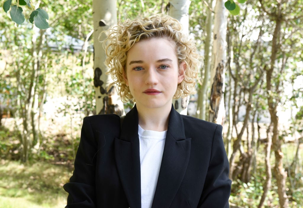 Julia Garner looking at the camera in front of a lightly wooded background