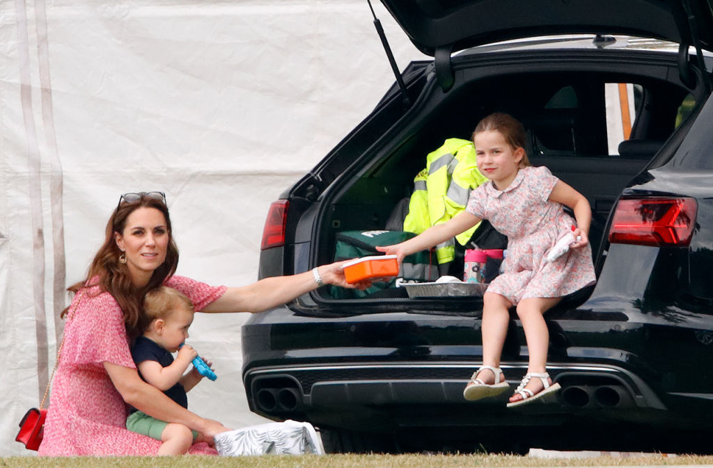 Kate Middleton sits with Prince Louis on her lap as she hands box to Princess Charlotte