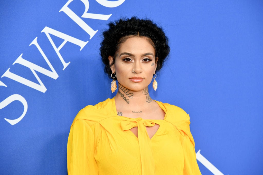 Kehlani smiling slightly wearing yellow in front of a blue background