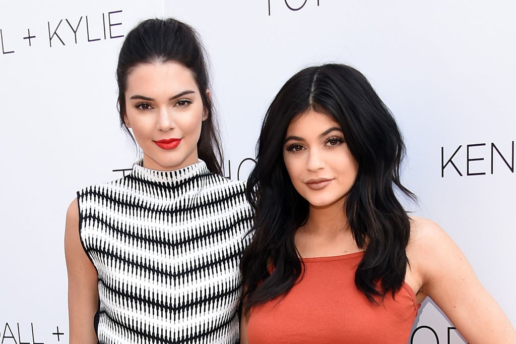 Kendall Jenner and Kylie Jenner smiling in front of a white background with a repeating logo
