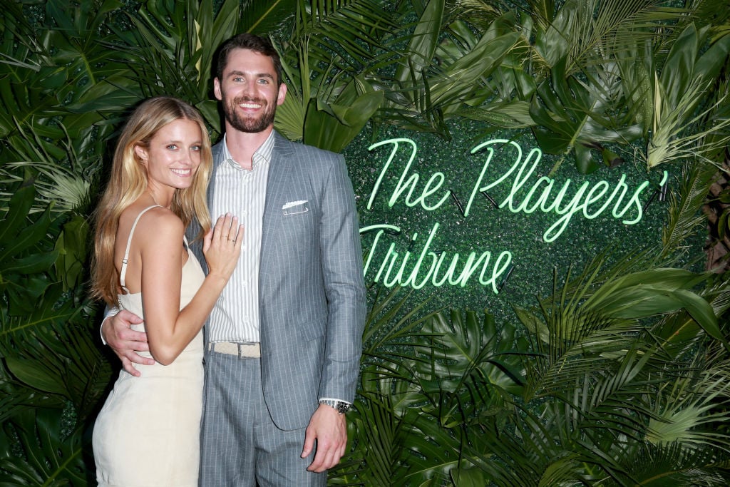 Kevin Love and Kate Bock smiling in front of a plant wall