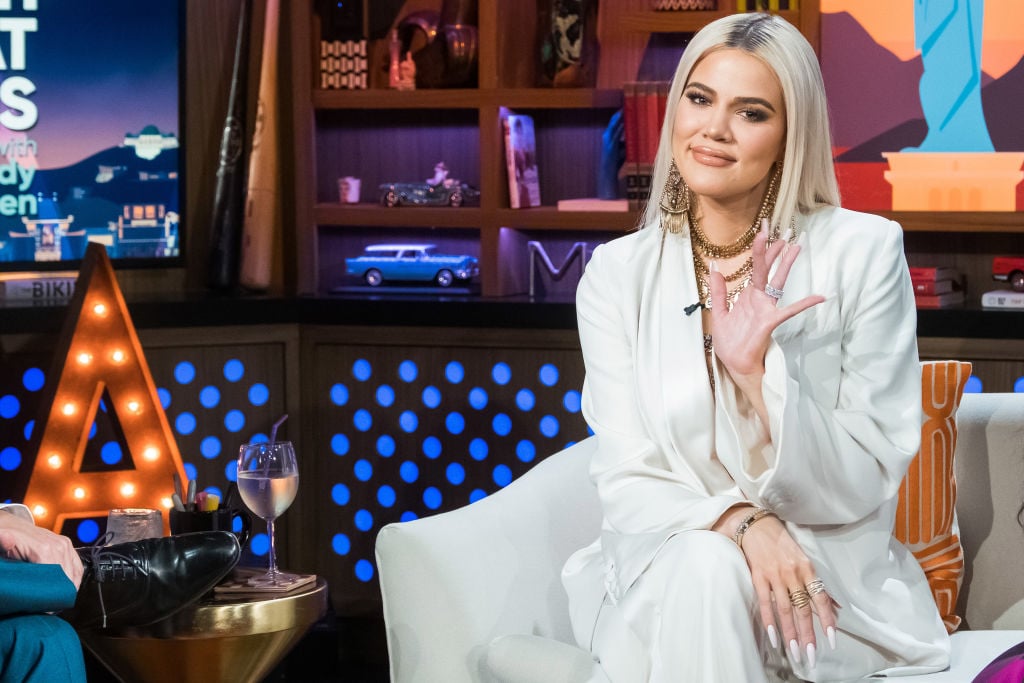 Khloé Kardashian smiling and waving while sitting on a couch