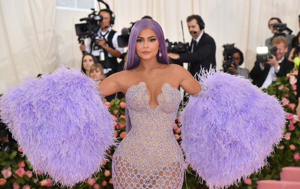 Kylie Jenner smiling slightly in a purple dress with giant fluffy arm gloves