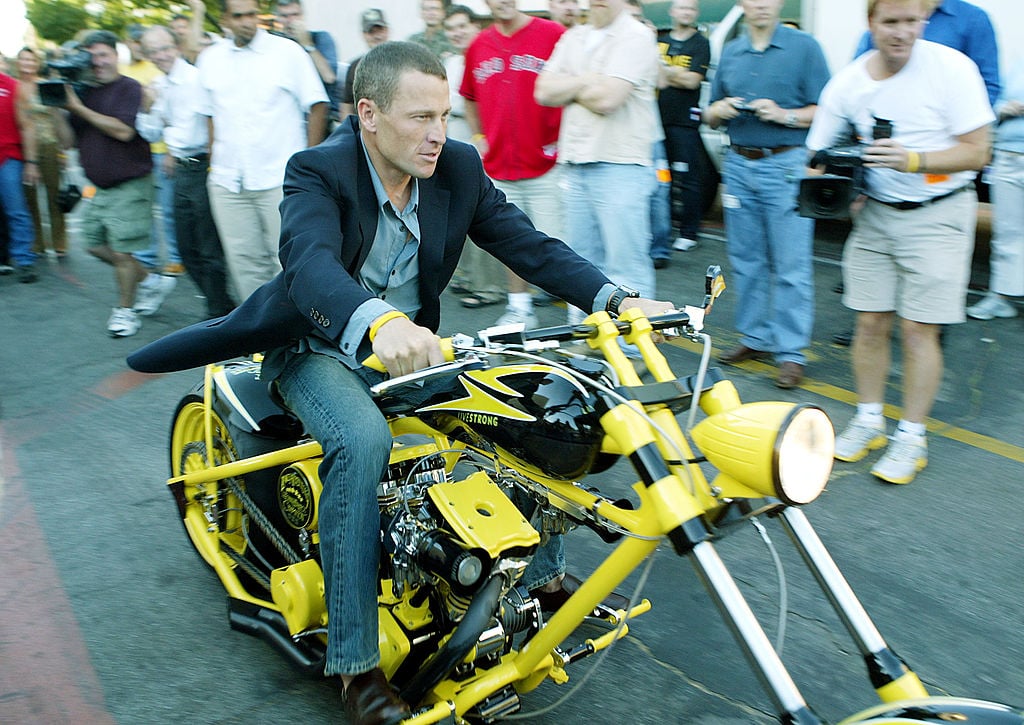 Lance Armstrong on a motorcycle smiling, slightly blurred