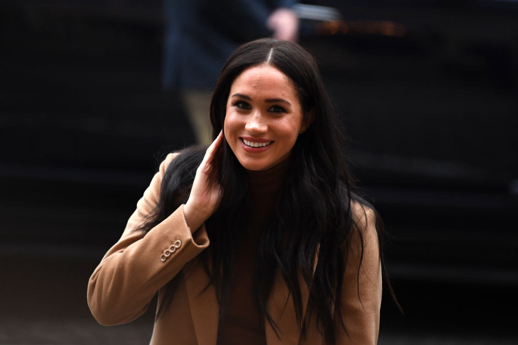 Meghan Markle smiling, pulling her hair behind her ear