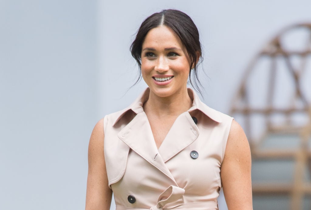 Meghan Markle smiling looking off camera in a tan buttoned shirt