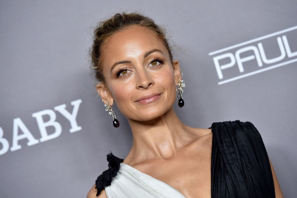 Nicole Richie smiling in front of a gray backdrop wearing black and white