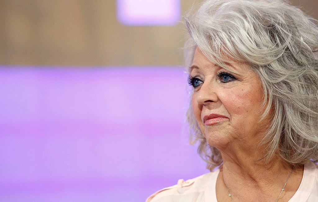 Paula Deen looking off camera in front of a light purple background