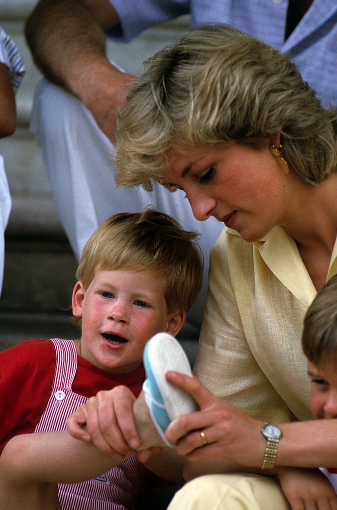 Princess Diana helps a young Prince Harry put his shoes on while on a family vacation in Spain, circa 1987