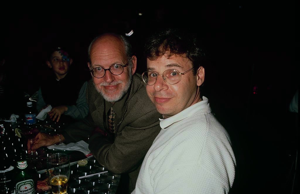 Rick Moranis smiling, looking sideways at the camera