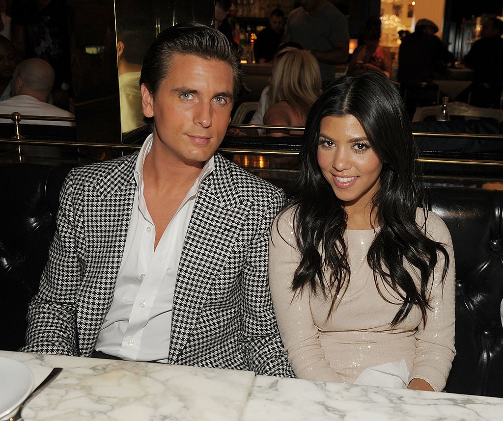 Scott Disick and Kourtney Kardashian smiling at the camera sitting at a table