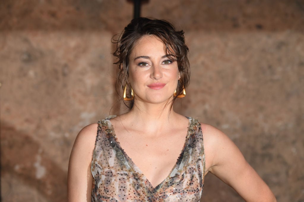 Shailene Woodley smiling at the camera in a beige and white dress