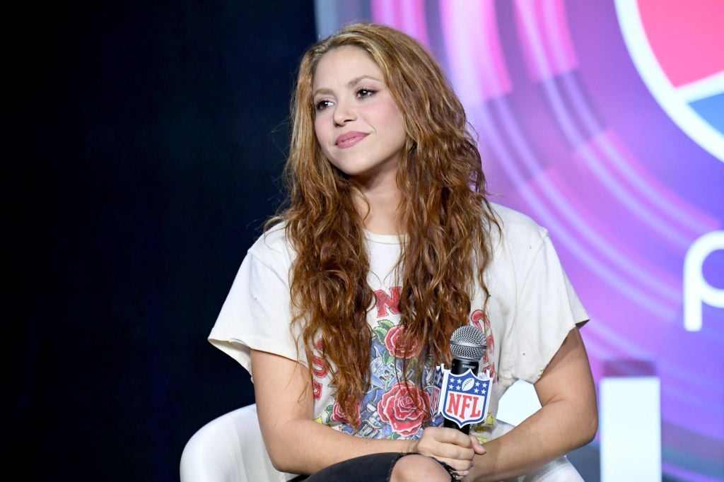 Shakira smiling holding a microphone with an NFL logo