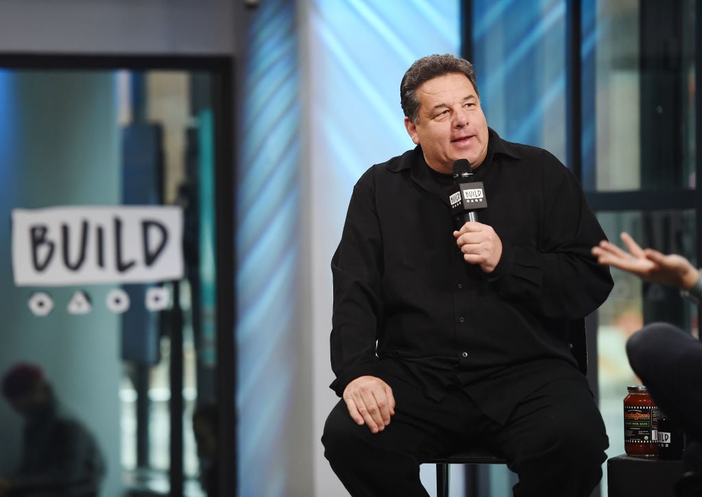 Steve Schirripa smiling, seated, holding a microphone