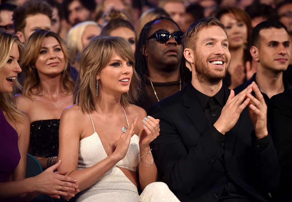 Taylor Swift and Calvin Harris smiling and clapping, sitting in a theater