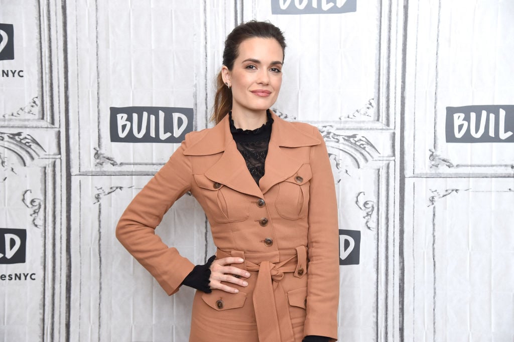 Torrey DeVitto smiling in front of a repeating background