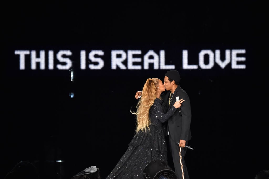 Beyoncé and Jay-Z kissing on stage in front of a background that says 'THIS IS REAL LOVE'