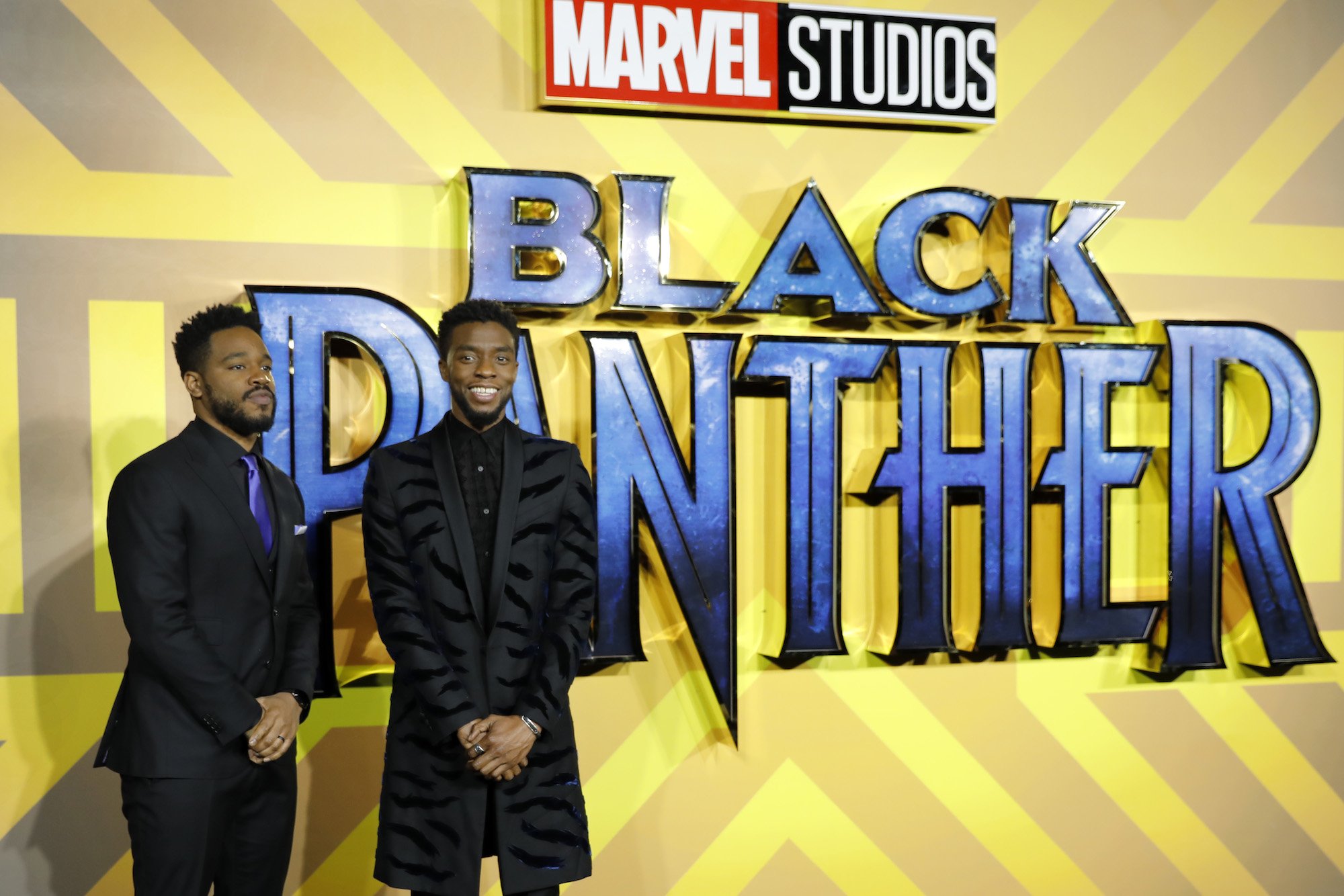 Ryan Coogler and Chadwick Boseman standing in front of a yellow background with a blue 'Black Panther' logo