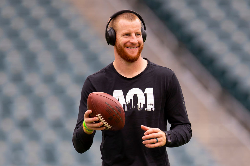 Carson Wentz smiling, holding a football wearing headphones