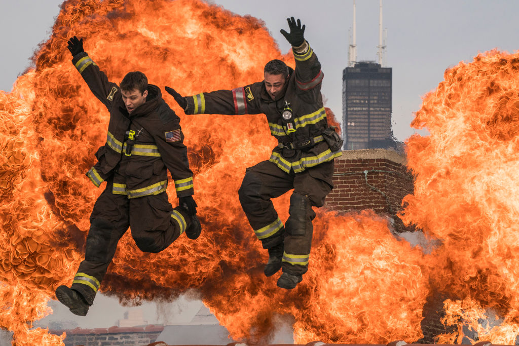 Jesse Spencer as Matthew Casey, Taylor Kinney as Kelly Severide jumping in front of large clouds of fire