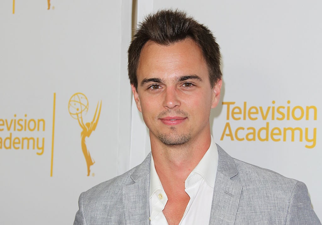 Darin Brooks smiling in front of a white background with a repeating logo