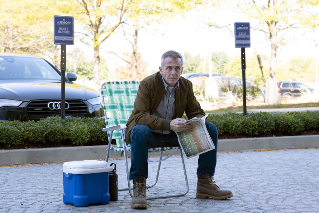 David Eigenberg as Christopher Herrmann sitting in a lawn chair holding a paper, looking off into the distance